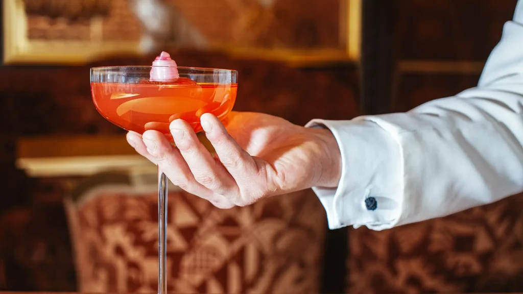Bartender serves a red cocktail in a coupe glass
